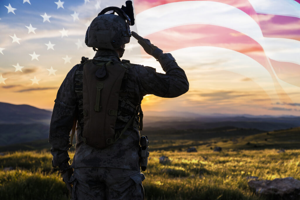 Soldier saluting a transparent US flag while facing the sunset